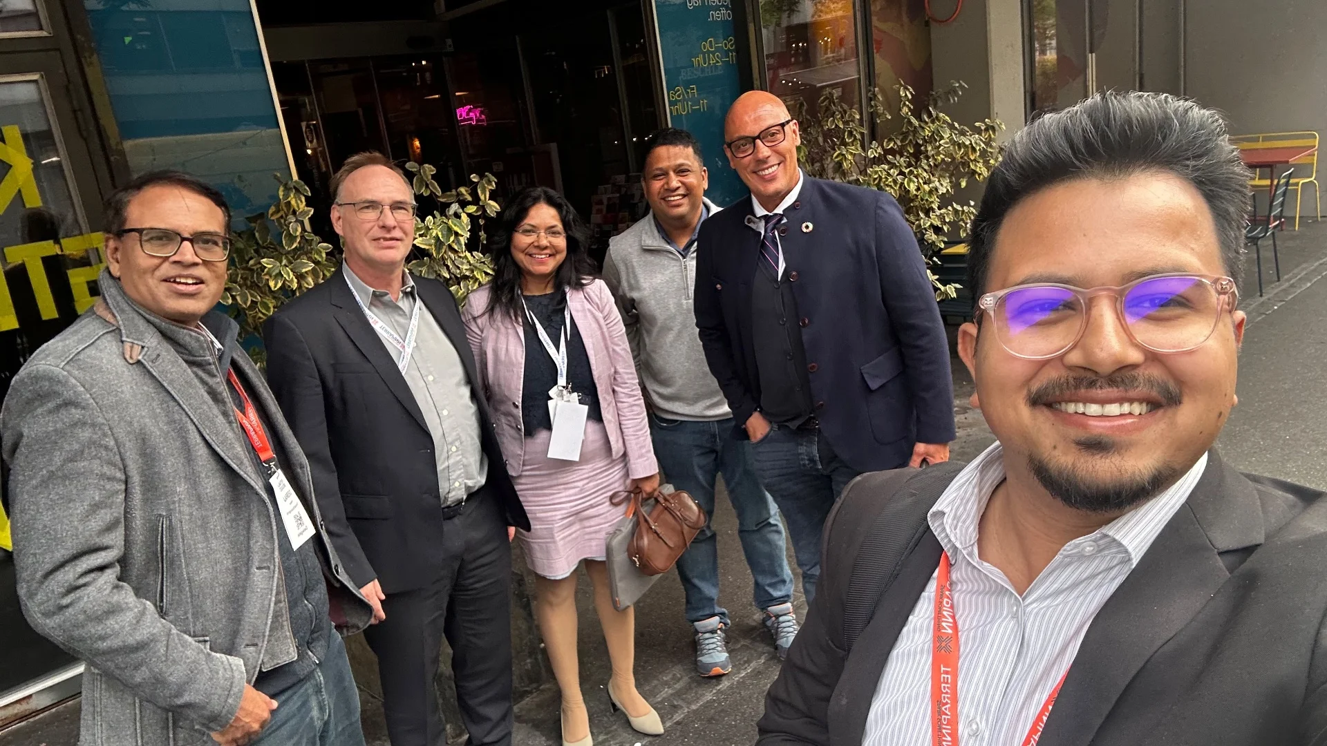 Group photograph of six people standing together outside on a street in Switzerland, smiling at the camera during collaborative discussions.